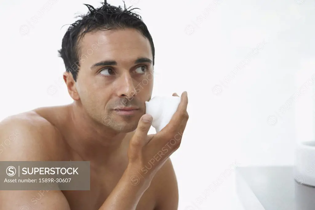 Man with bare chest applying shaving cream to face
