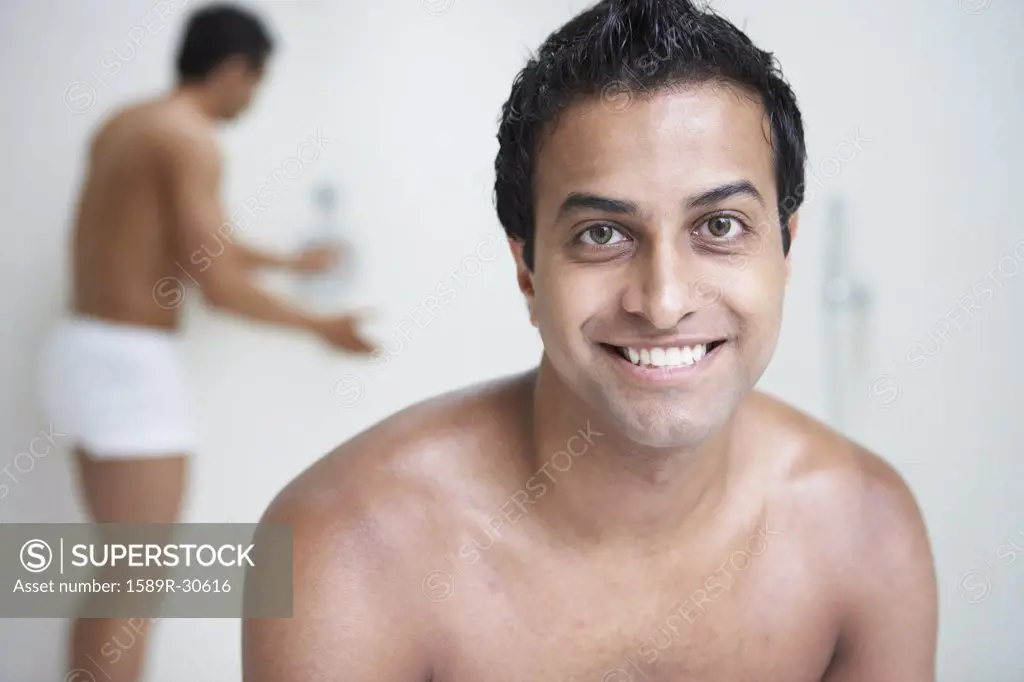 Indian man with bare chest smiling while man in underwear tests shower in  background - SuperStock