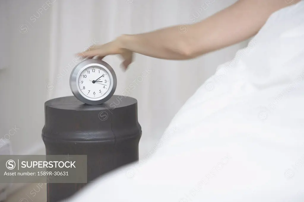 Woman reaching for alarm clock from bed