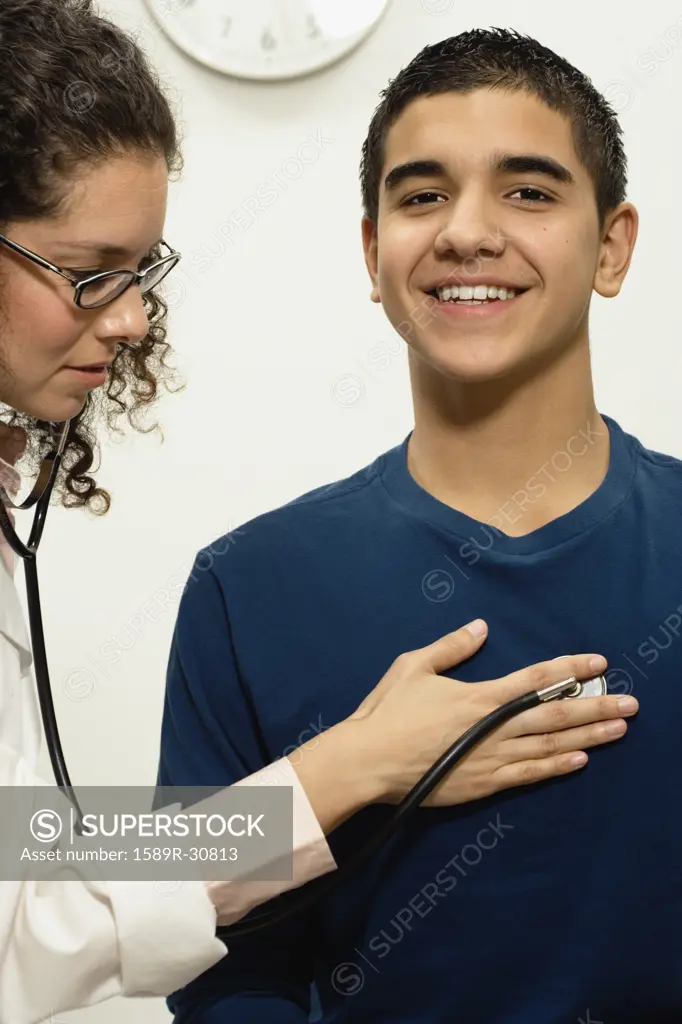 Female doctor checking young male patient with stethoscope