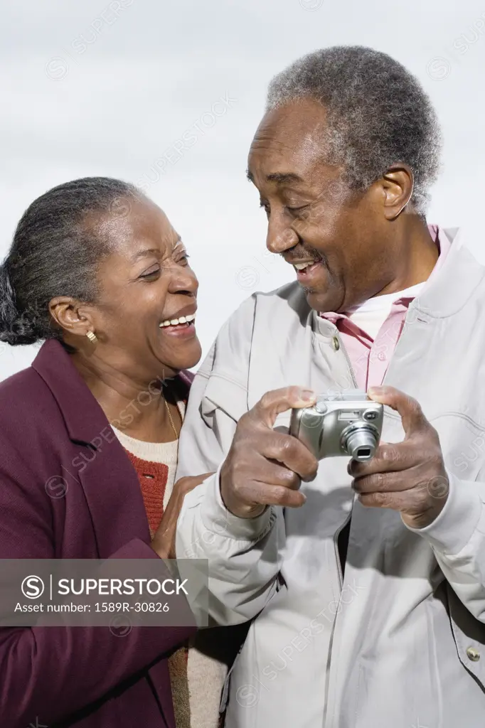 Senior African couple with digital camera smiling at each other