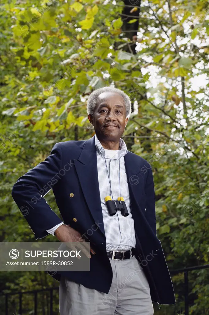 Senior African man with binoculars around neck in woods