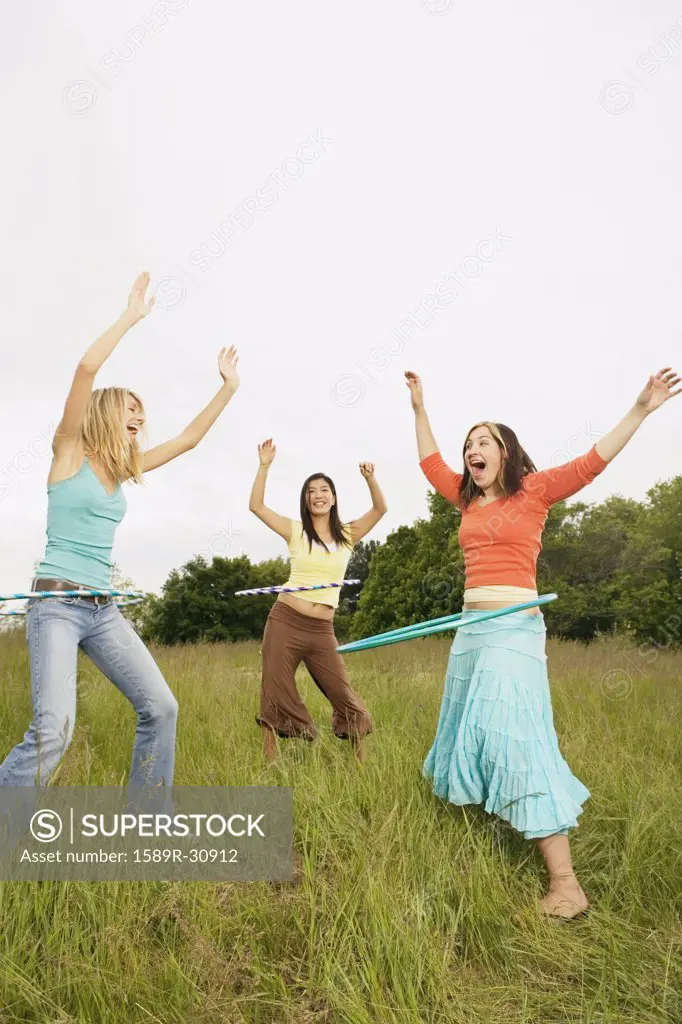 Three young women playing with hula hoops in meadow
