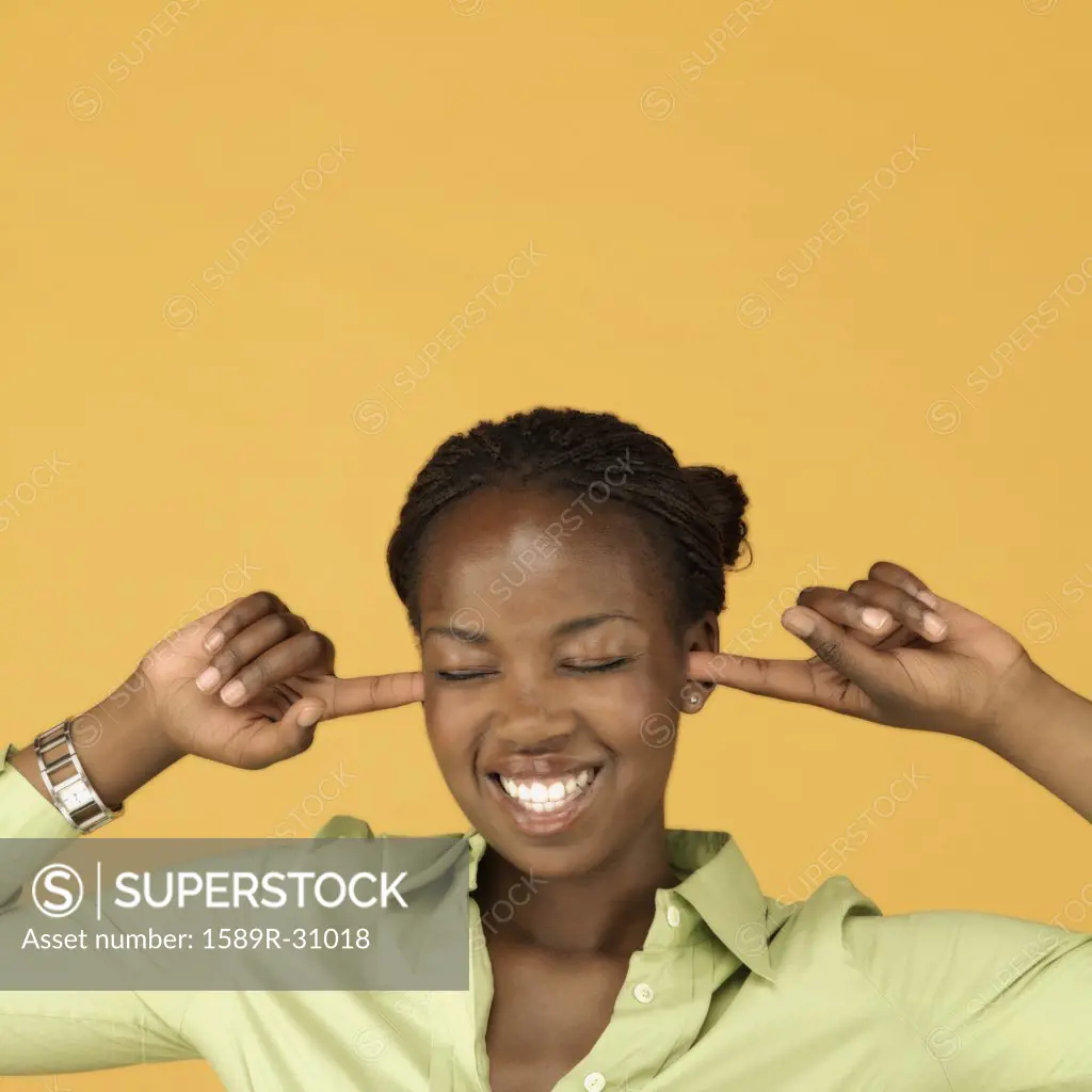 Studio shot of African woman plugging ears with fingers