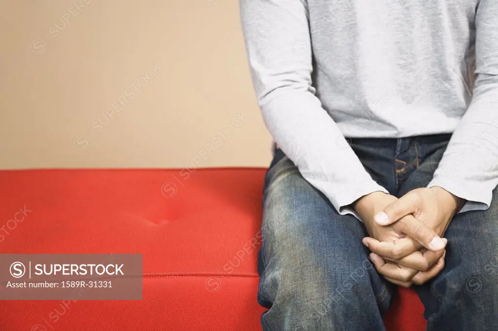Close up of man sitting on sofa with hands clasped