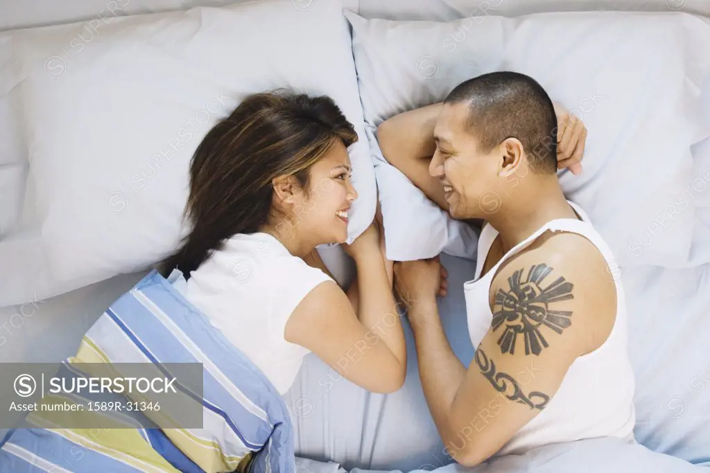High angle view of Asian couple smiling at each other in bed