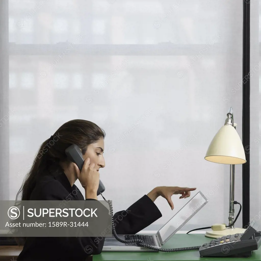 Indian businesswoman using laptop and telephone indoors