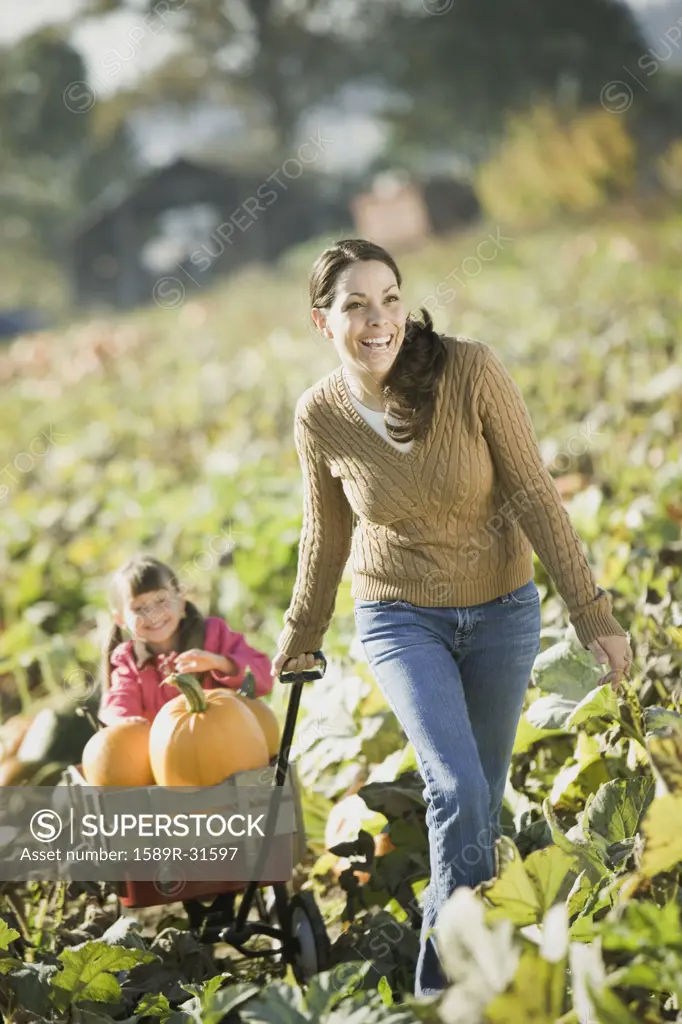 Hispanic mother pulling daughter in wagon through pumpkin patch