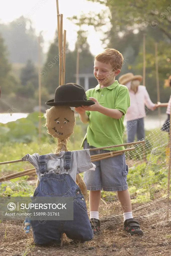 Young boy putting hat on scarecrow