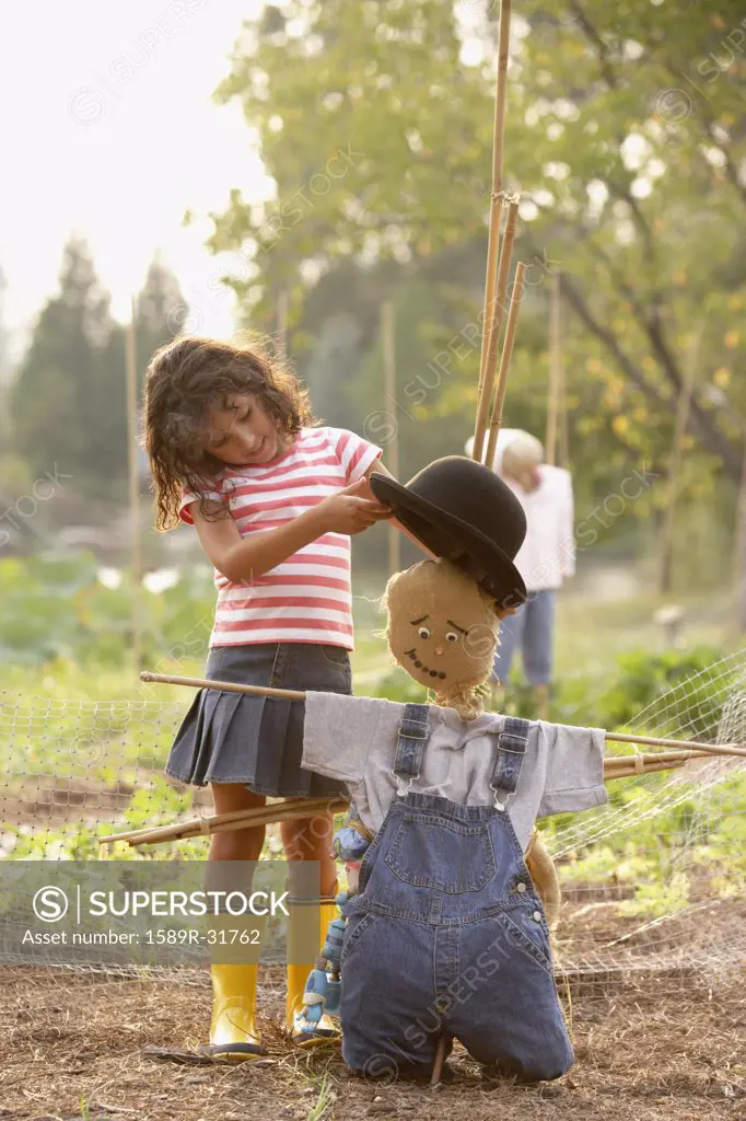 Young Hispanic girl putting hat on scarecrow