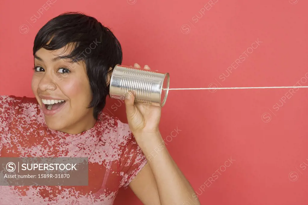 Hispanic woman holding can with string to ear