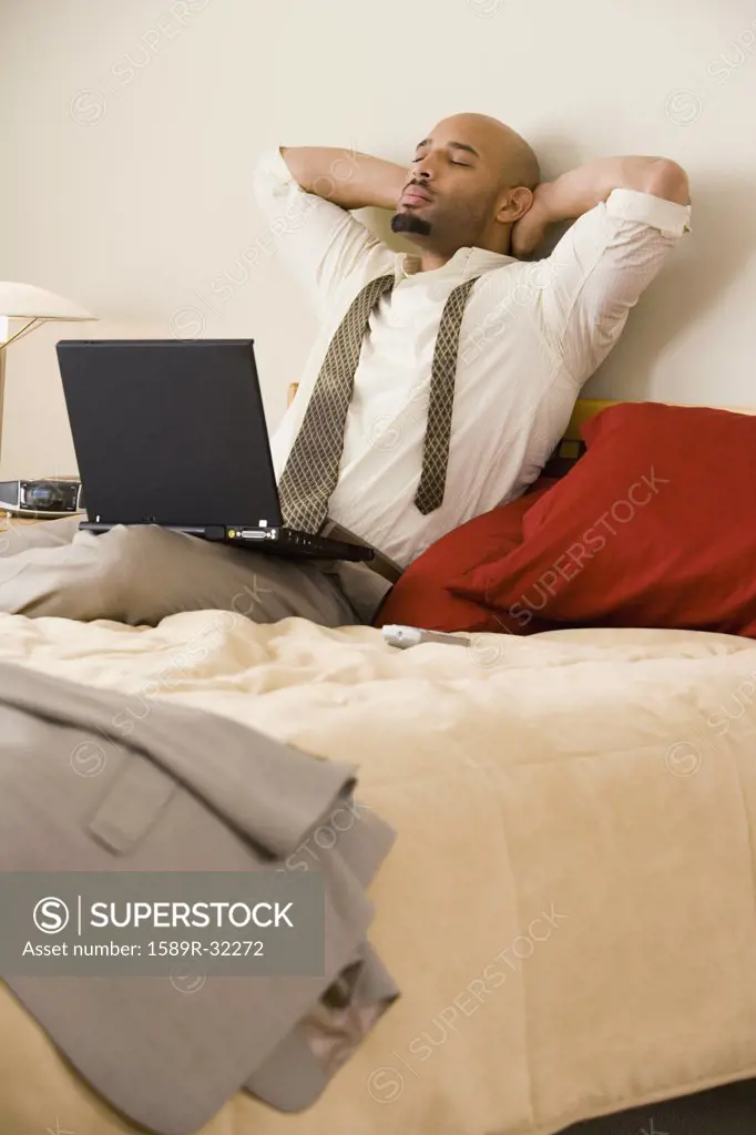 African businessman relaxing on bed with laptop