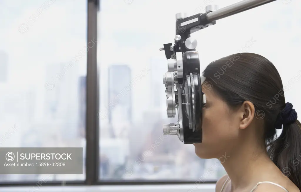 Profile of Asian womans face behind ophthalmology equipment
