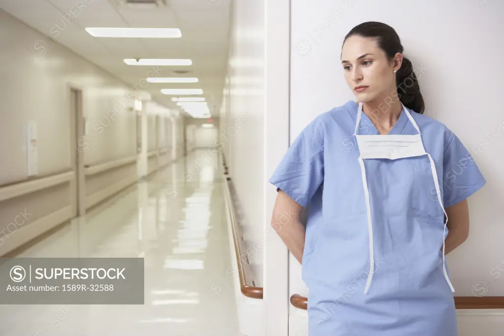 Female doctor leaning against wall in hospital corridor