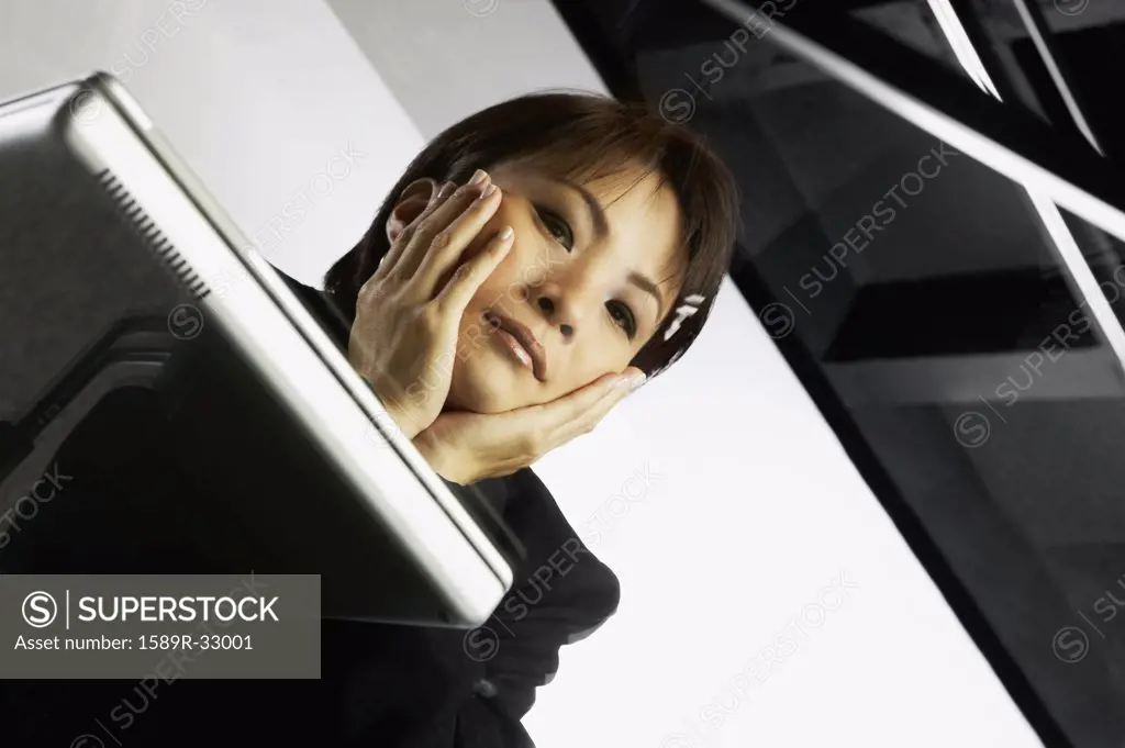 Low angle view through glass desk of Asian businesswoman and laptop