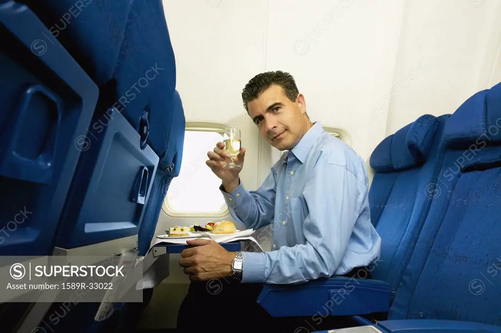 Man eating and toasting with wine on airplane