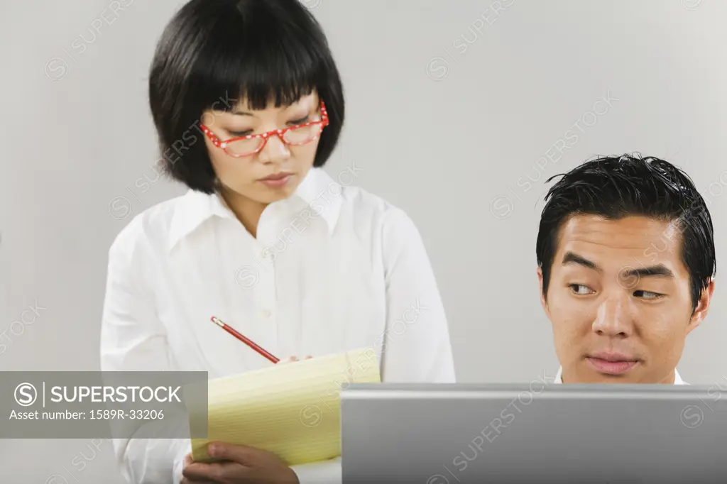 Asian woman taking notes next to man at computer