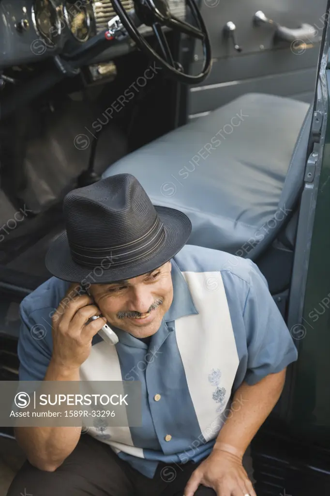 Middle-aged Hispanic man talking on cell phone in classic car