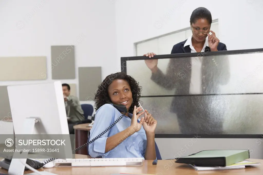 African businesswoman filing fingernails with boss watching