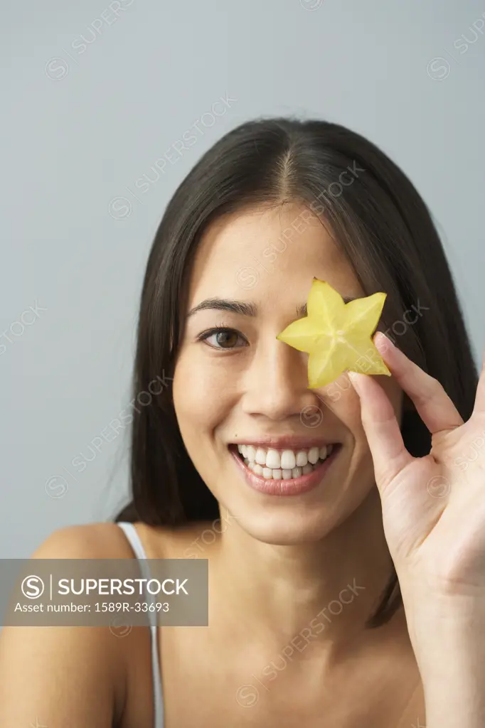 Asian woman holding star fruit over eye