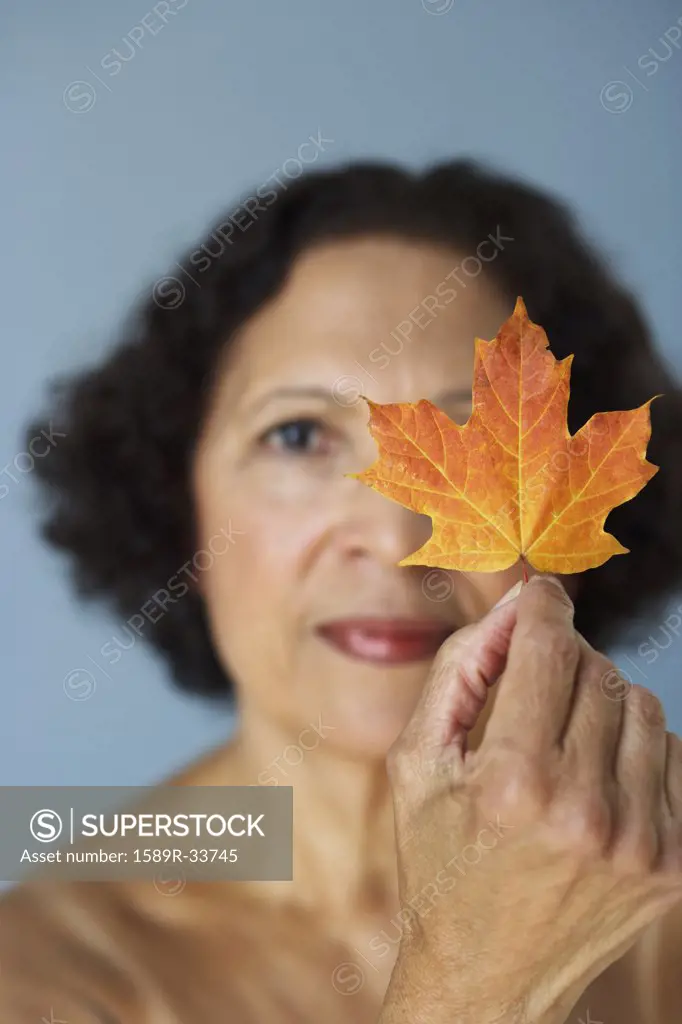 Senior African woman holding autumn leaf over eye