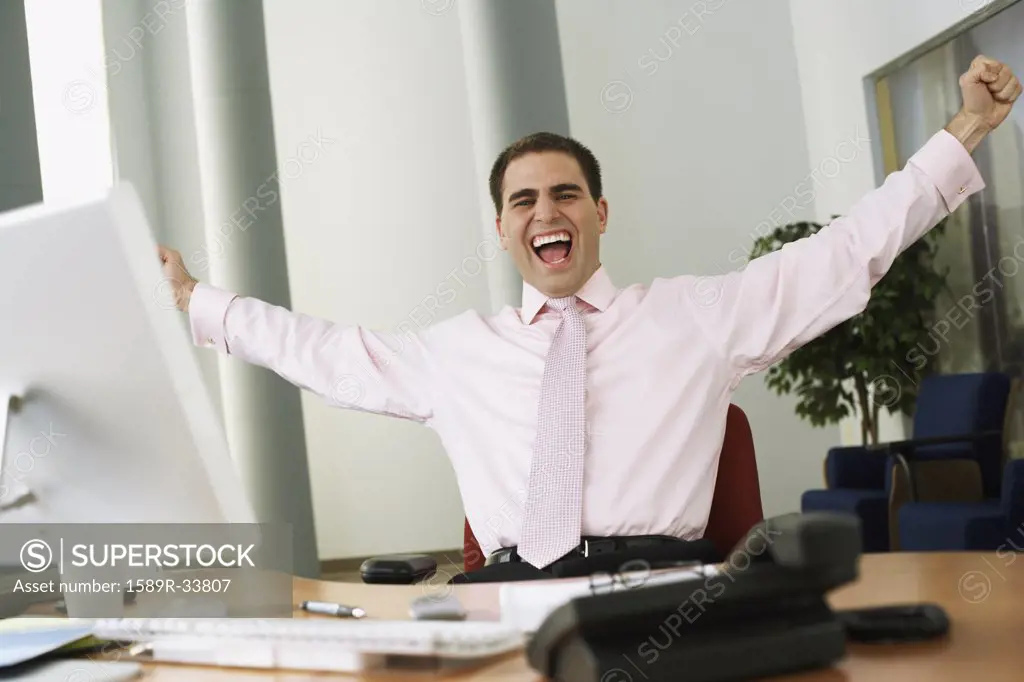 Middle Eastern businessman cheering at desk