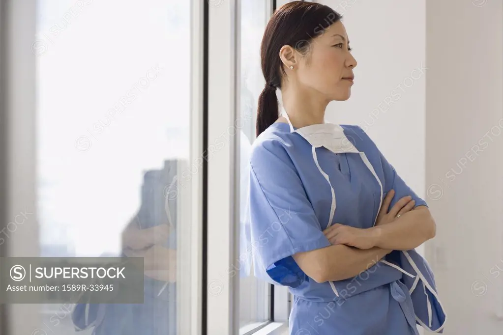 Asian female doctor leaning against window with arms crossed