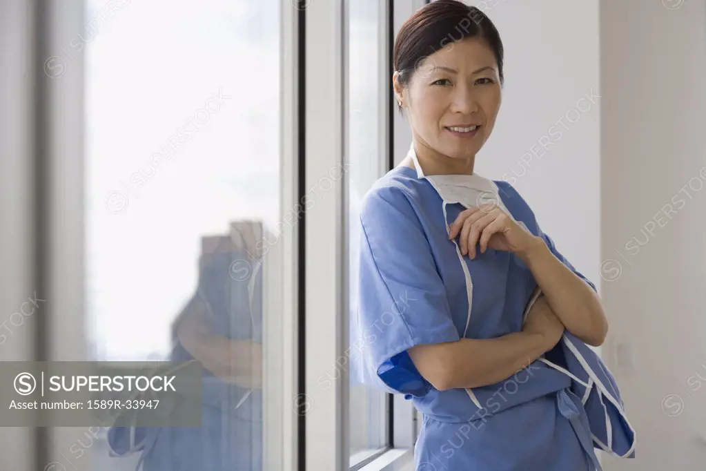 Asian female doctor leaning against window smiling