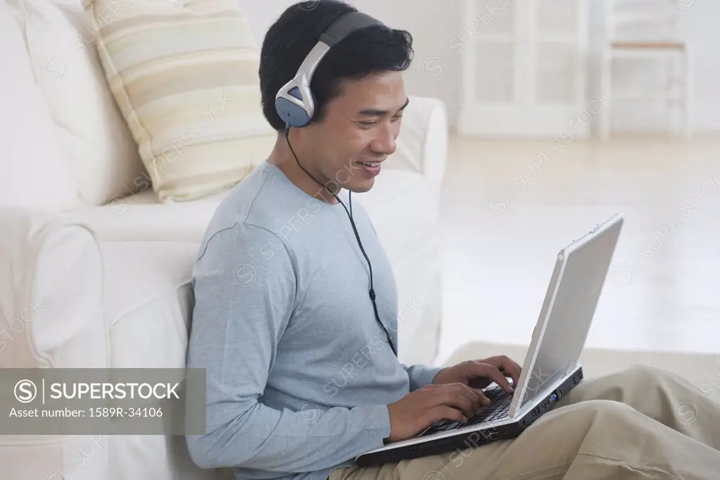 Asian man using laptop with headphones
