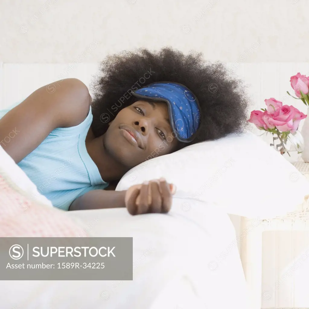 African woman wearing eye mask in bed
