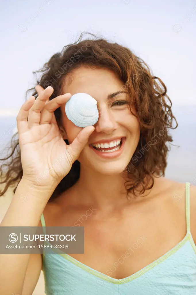 Woman holding seashell over eye