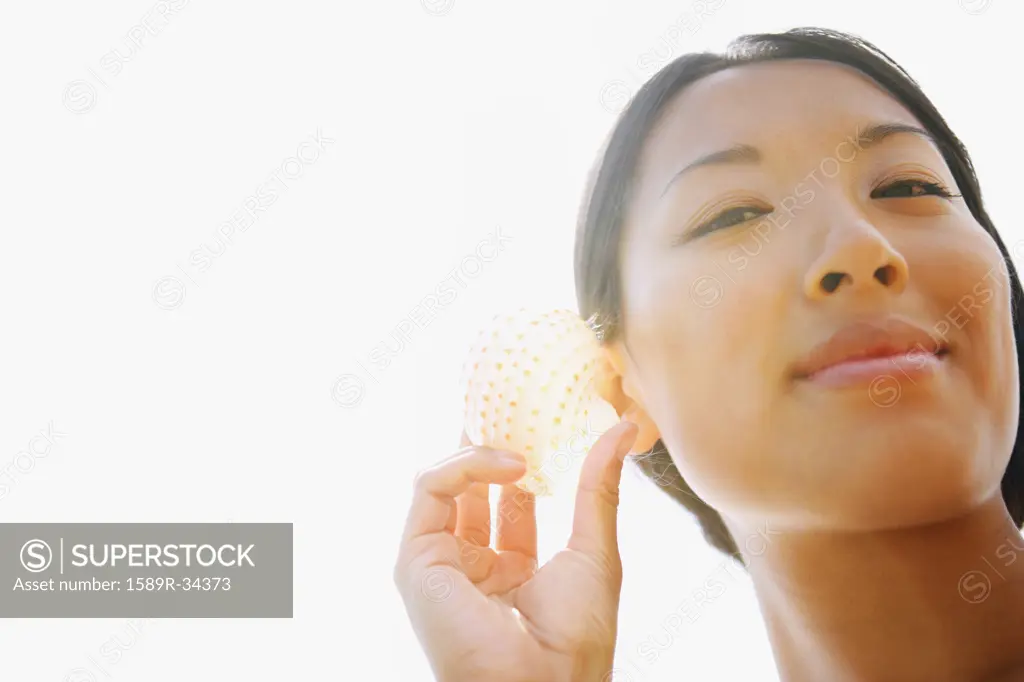 Asian woman listening to seashell