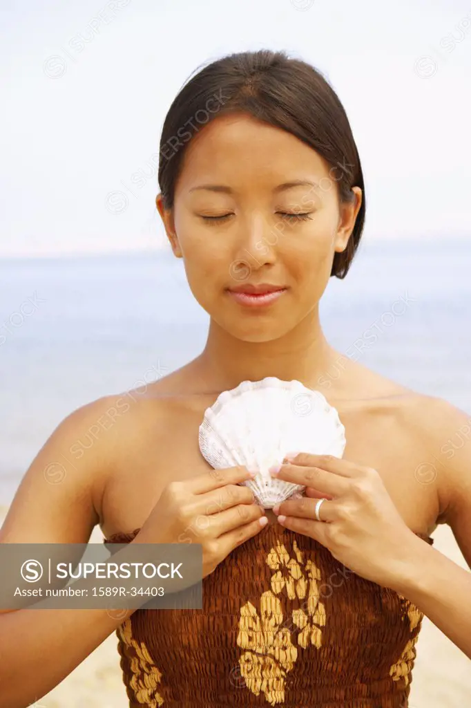 Asian woman holding seashell against chest