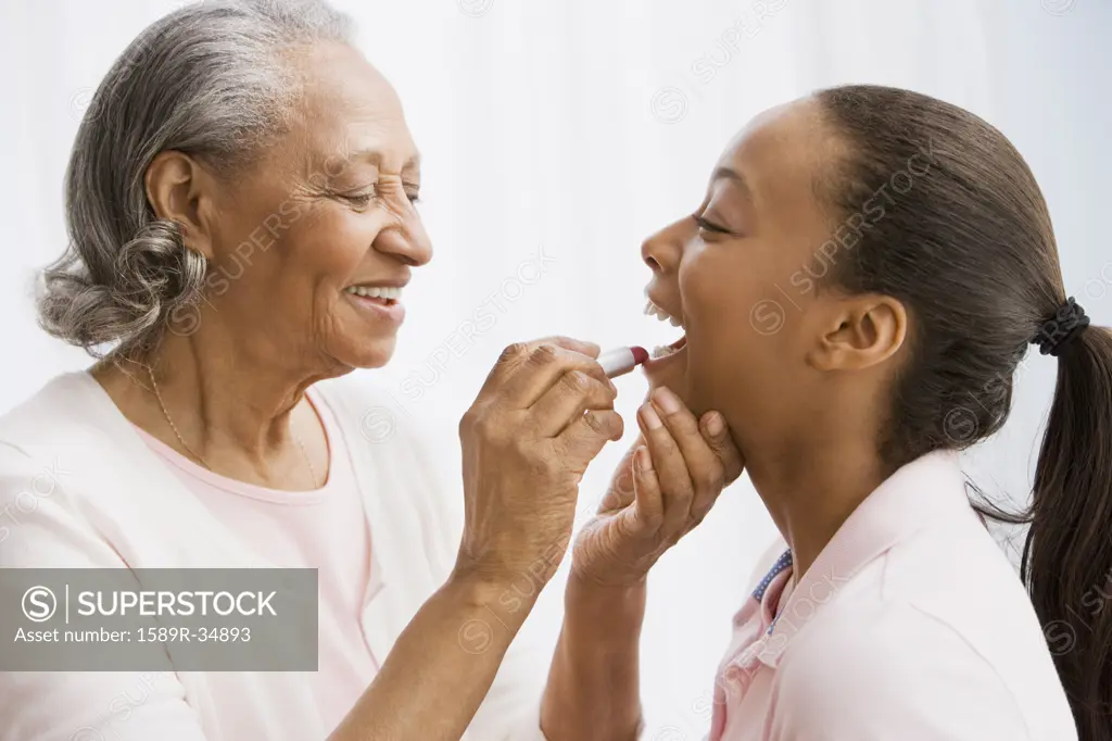 African grandmother helping granddaughter apply lipstick