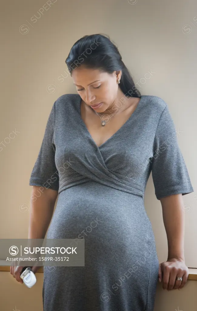 Pregnant Hispanic woman leaning against wall