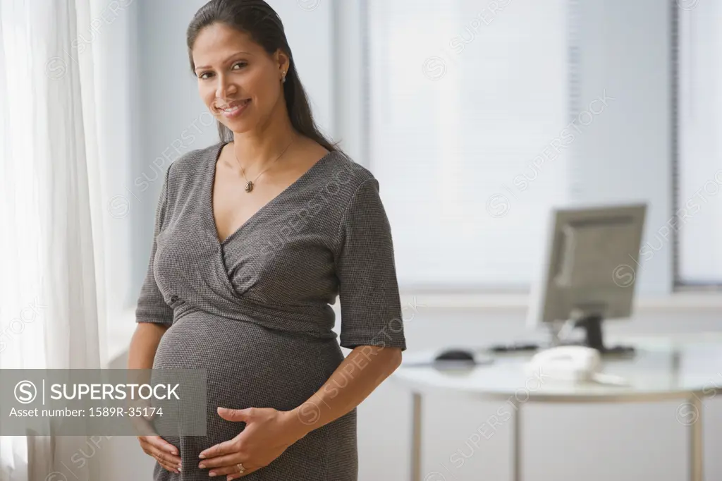 Pregnant Hispanic businesswoman standing in office
