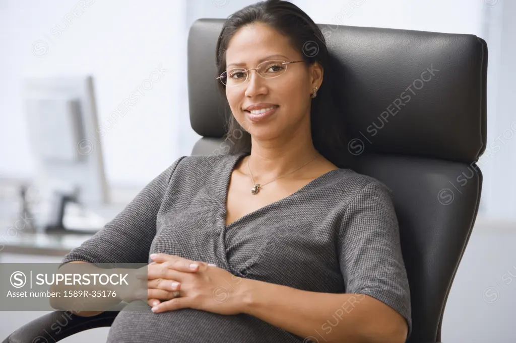 Pregnant Hispanic businesswoman sitting in office chair