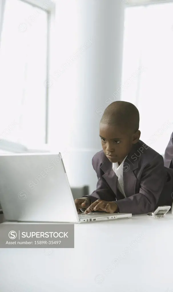 African boy in business suit using laptop in conference room