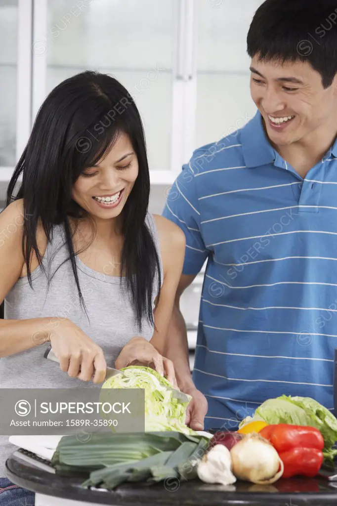 Asian couple chopping vegetables in kitchen