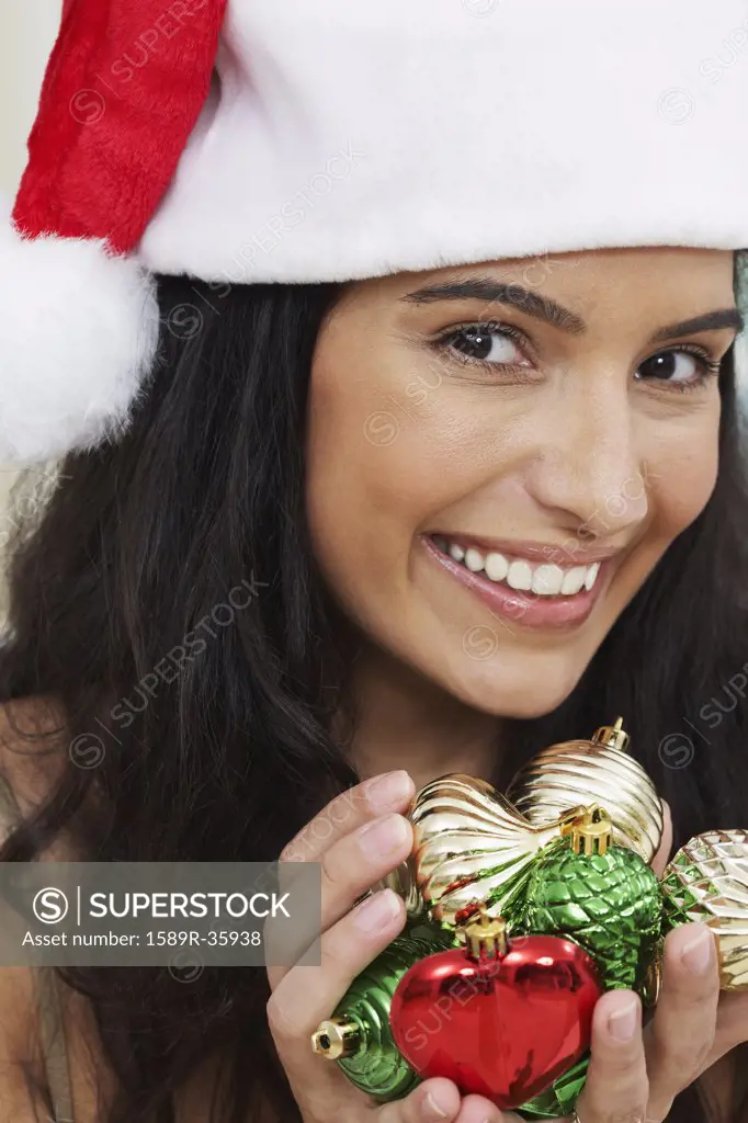 Hispanic woman wearing Santa hat and holding Christmas ornaments