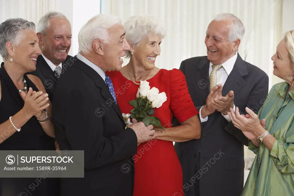 Senior man giving wife bouquet of flowers while friends clap