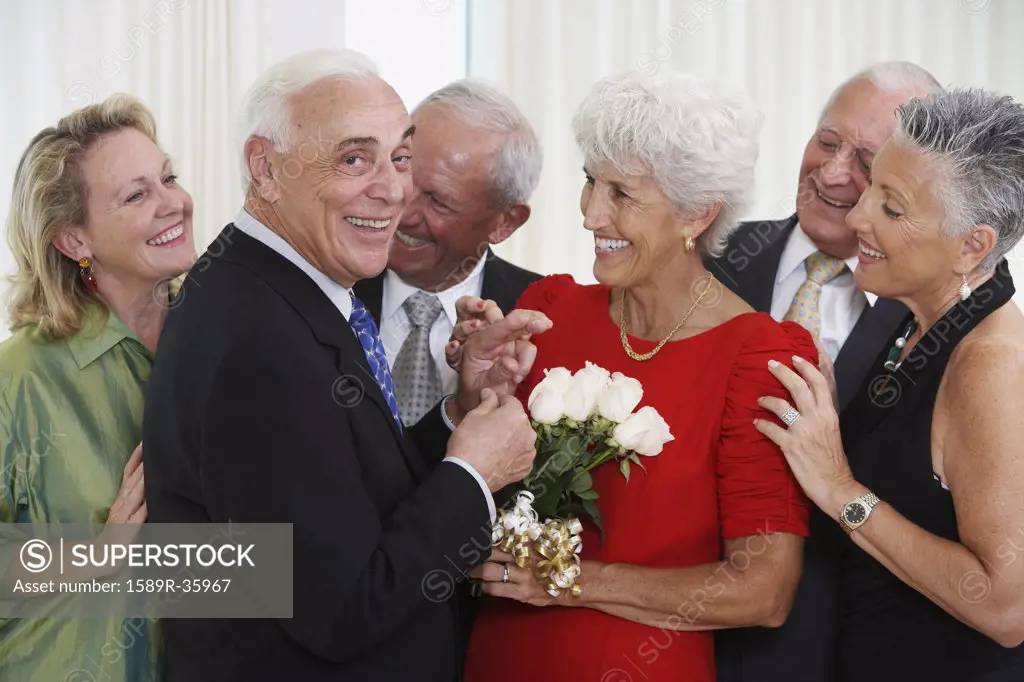 Senior man giving wife bouquet of flowers while friends watch