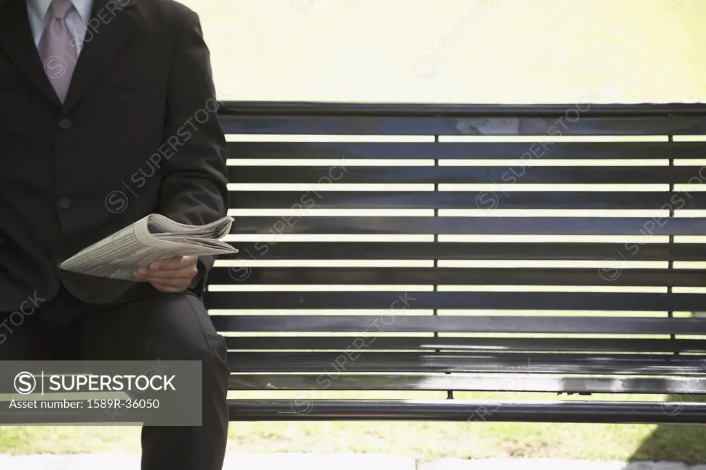 Businessman reading newspaper on park bench