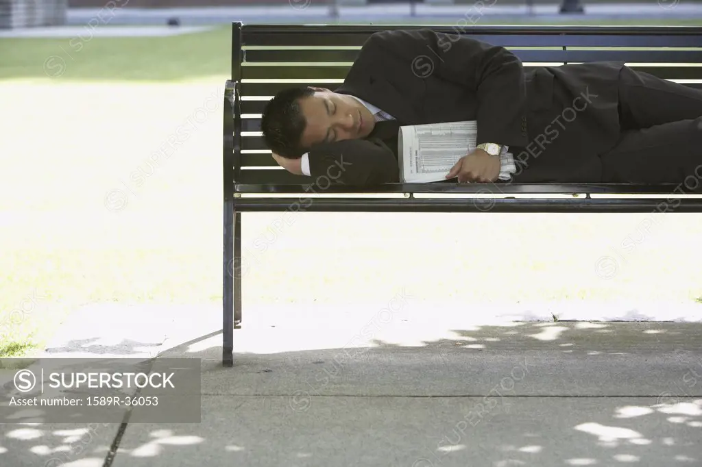 Asian businessman sleeping on park bench