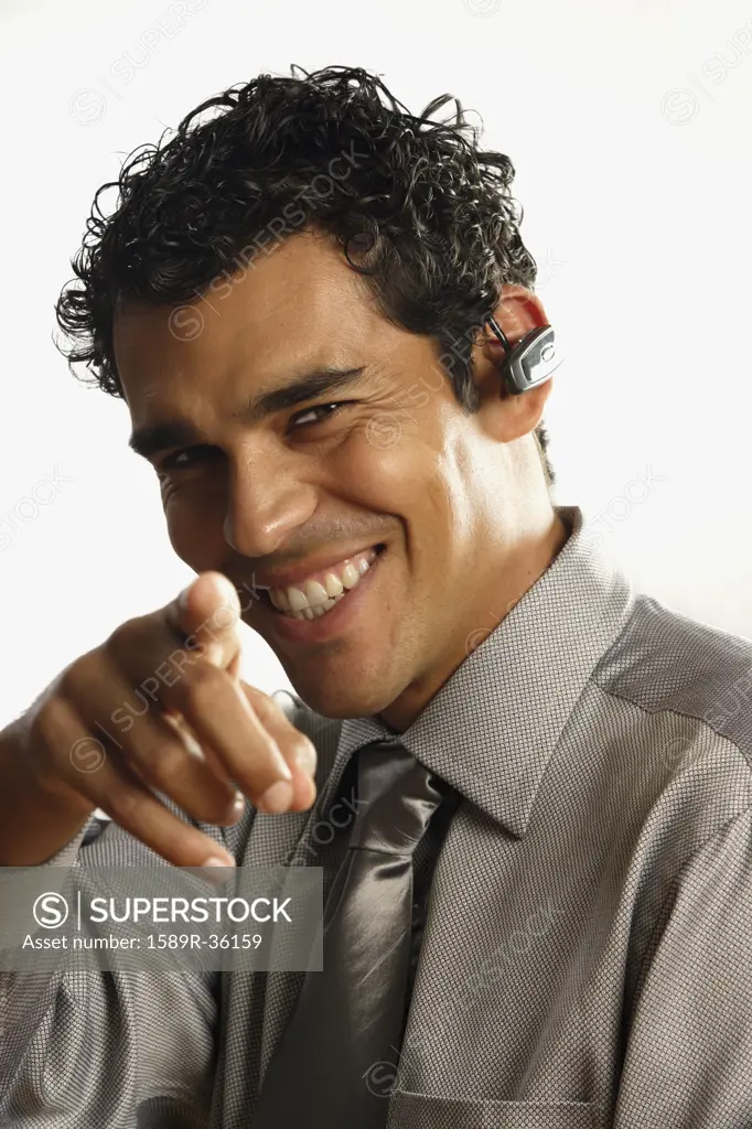 Studio shot of pointing Hispanic businessman with wireless earpiece