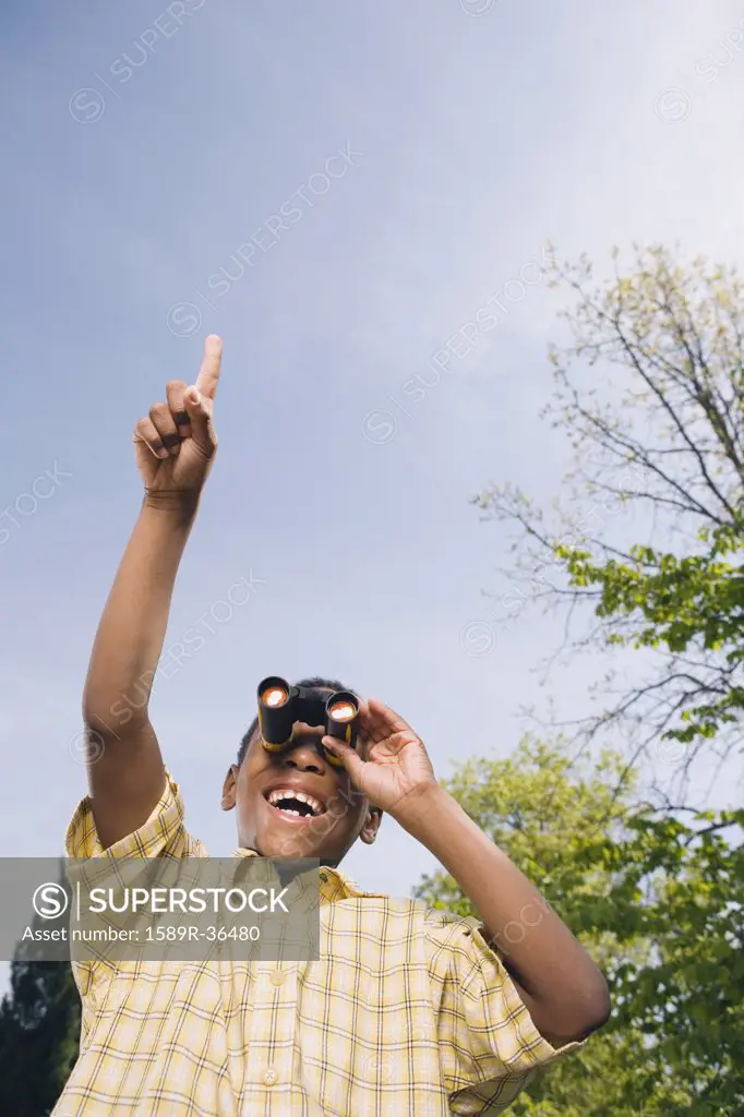 African boy with binoculars and pointing in park