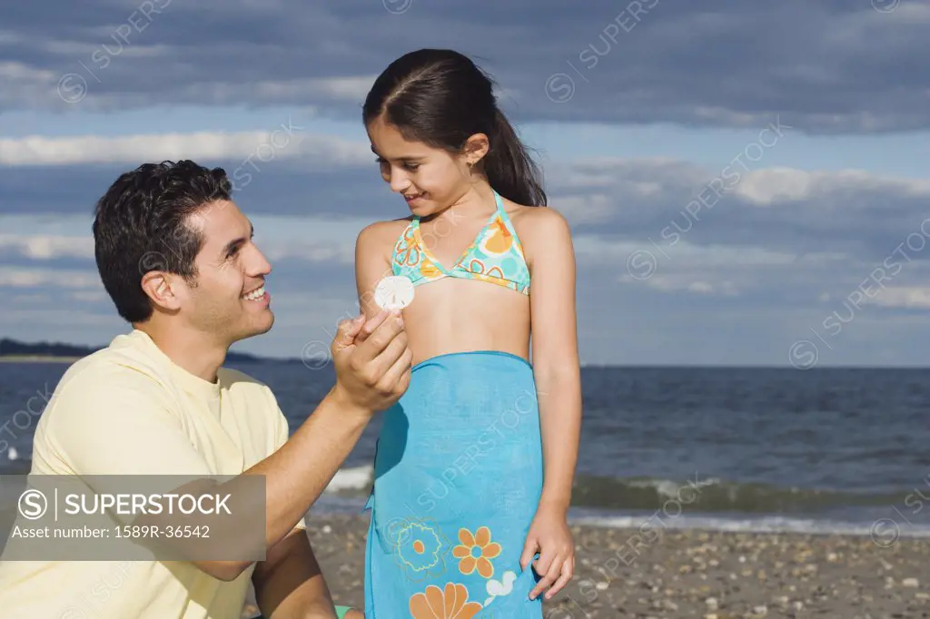 Hispanic father and daughter looking at seashell