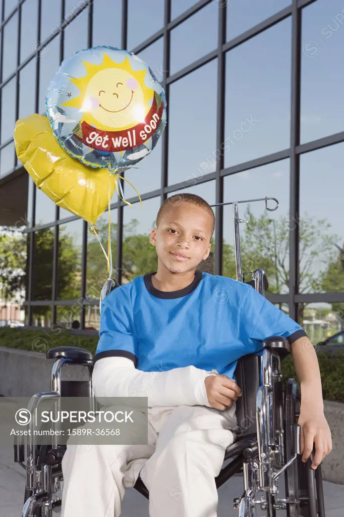 African boy with broken arm and balloons in wheelchair