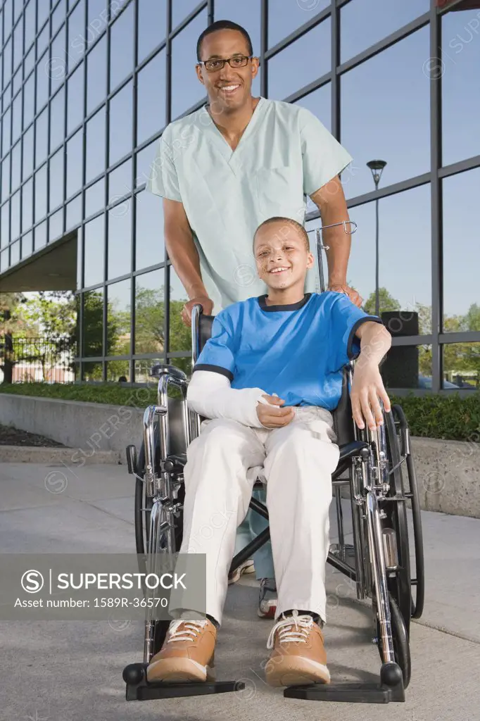 African boy in wheelchair with nurse in front of hospital
