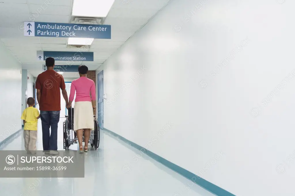 Rear view of African family walking down hospital corridor with wheelchair
